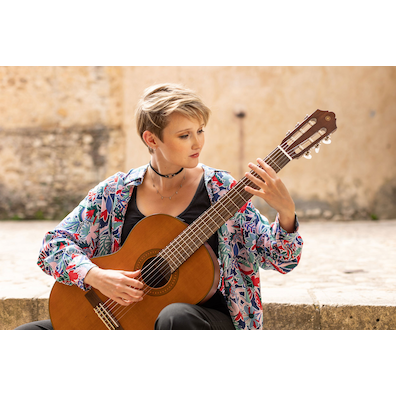 Stephanie Jones playing a CGX122MC while seated on stone steps in a courtyard of Pedraza, Segovia