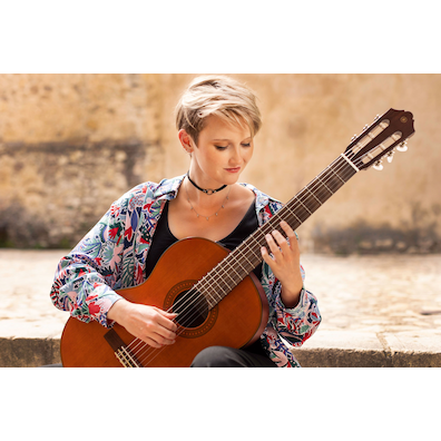 Stephanie Jones playing a CGX122MC while seated on stone steps in a courtyard of Pedraza, Spain