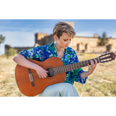 Stephanie Jones playing a CGX122MC sitting on a stool in a field in front of the Castillo de Pedraza