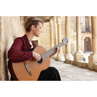Stephanie Jones sitting playing a CGX122MC with a view of the columns at the Plaza Mayor in Pedraza