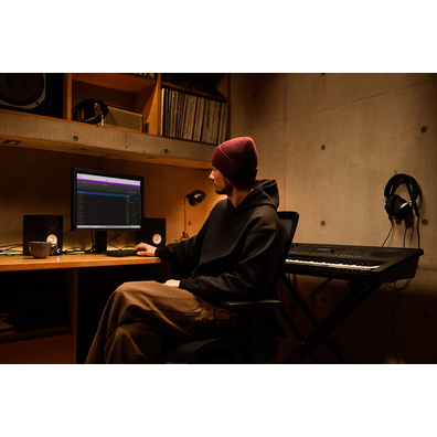 A home music workspace with a computer and keyboard, featuring a keyboardist working in their home studio