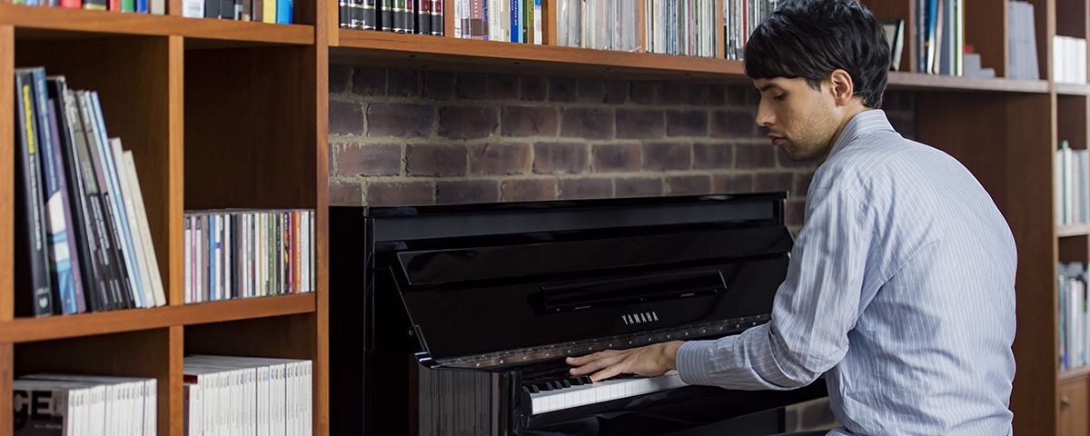 A man playing the AvantGrand NU1X piano in a nice living room