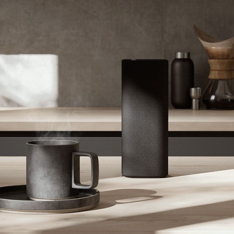 True X speaker on top of a kitchen table beside a coffee mug