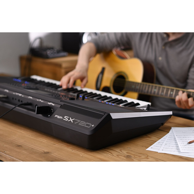 Photo of a person playing Yamaha Arranger Workstation PSR-SX720+ while holding a guitar