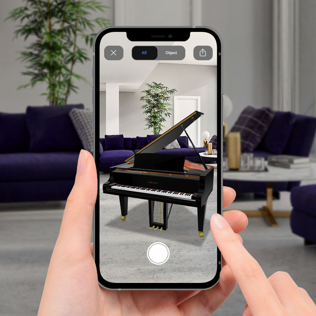 Image of a hand holding a phone and using augmented reality feature to view the piano in a room 
