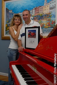 Joseph Poggioli and his wife stand behind their Elton John red piano.