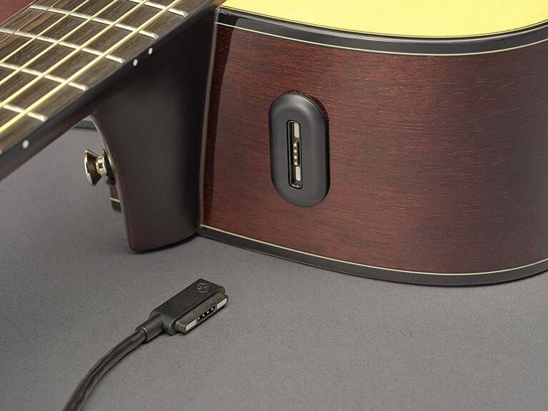 A close-up of the shoulder of the guitar detailing the connection for the charging cable to the rechargeable battery.  The neck heel strap button is visible.