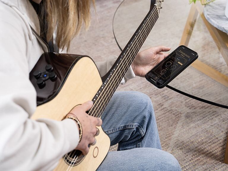 An over-the-shoulder shot of a seated woman holding the TAG3 C on her knee while adjusting the controls on the TAG Remote app on an iPhone.