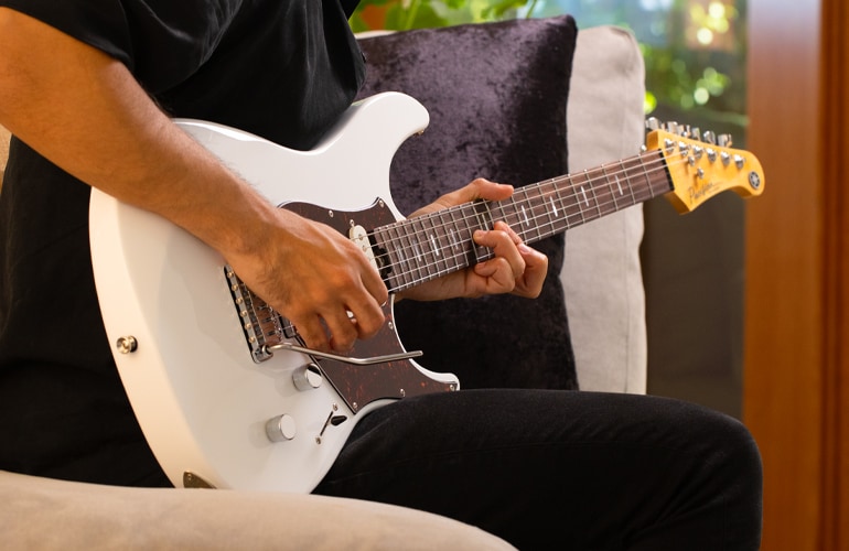 Closeup of male guitarist playing Shell White Pacifica Professional in home environment.